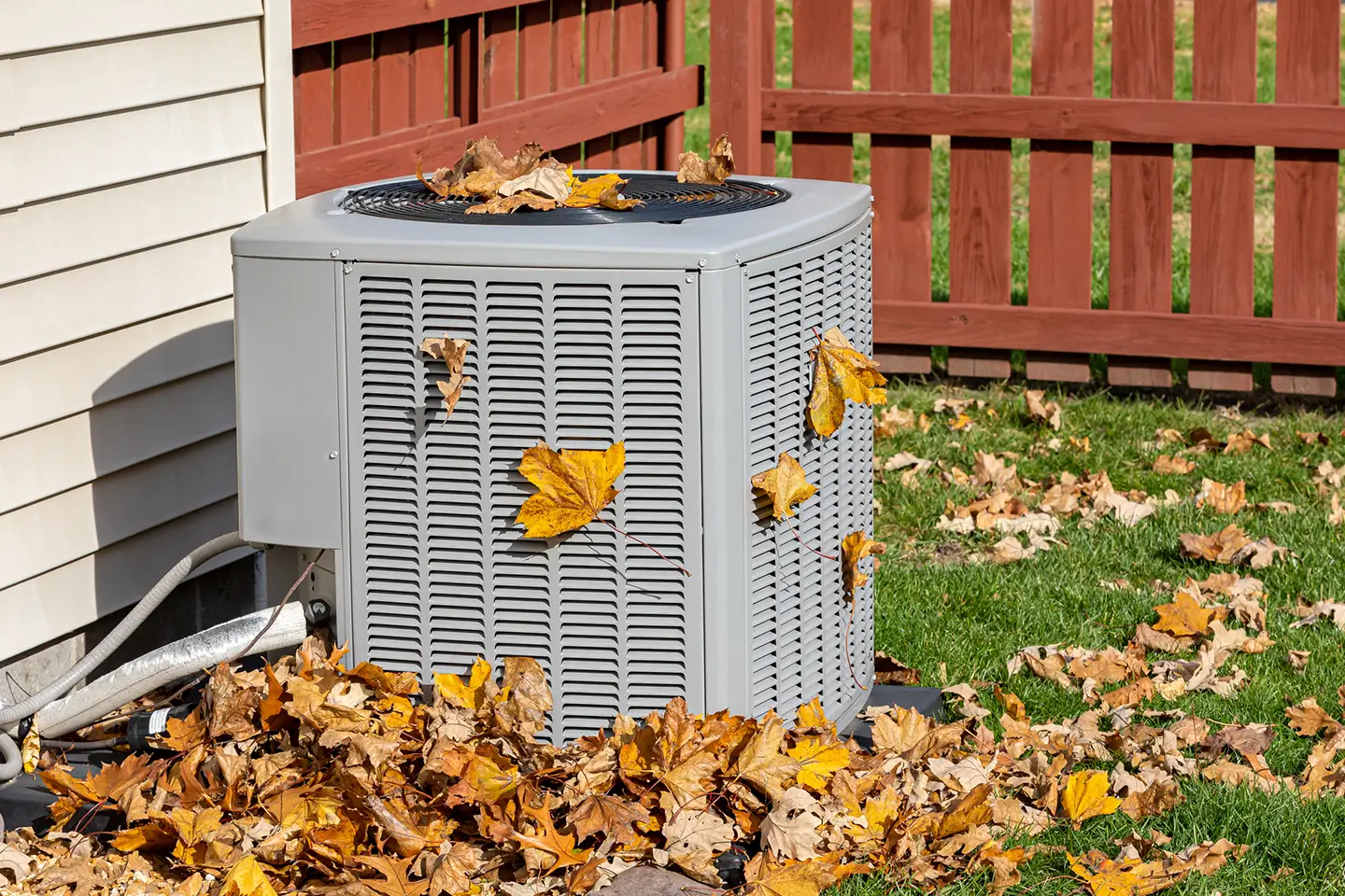 Outdoor air conditioner unit surrounded by fallen autumn leaves during the late-season installation window