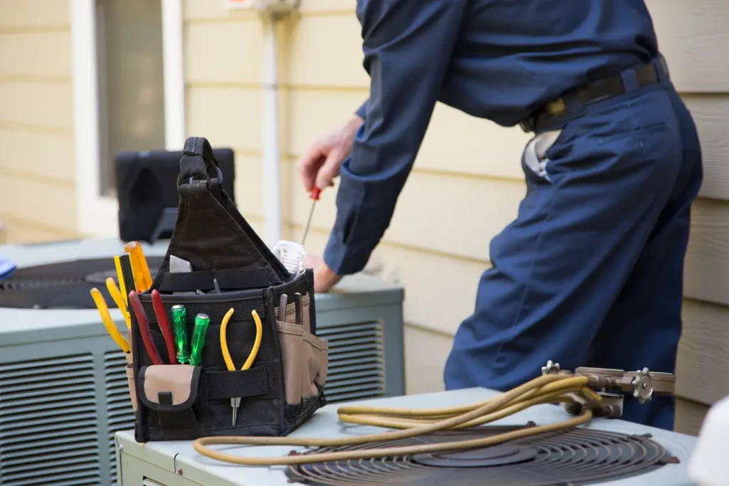 HVAC technician with a tool bag working on an outdoor air conditioning unit