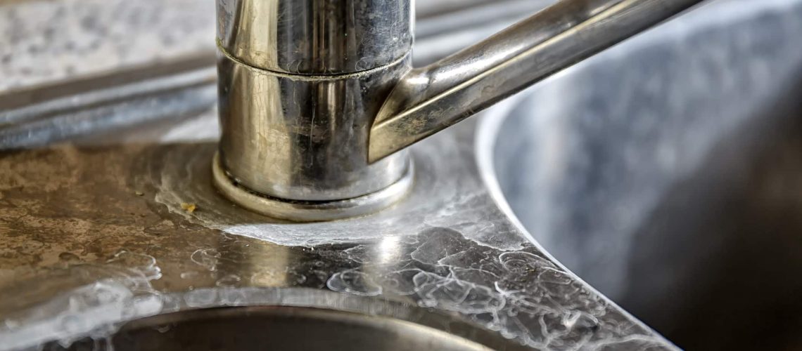 Close-up of a kitchen tap and sink with hard water calcification.