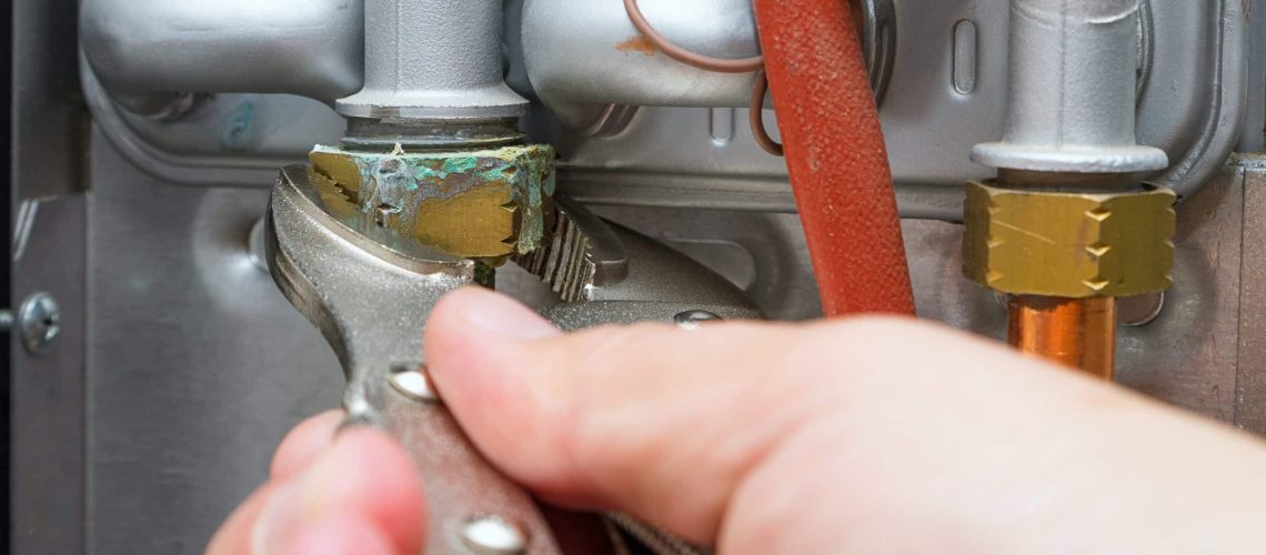 Servicing a heating home system.Technician with wrench repairs leaked hot water pipe in gas boiler. Close-up, selective focus.