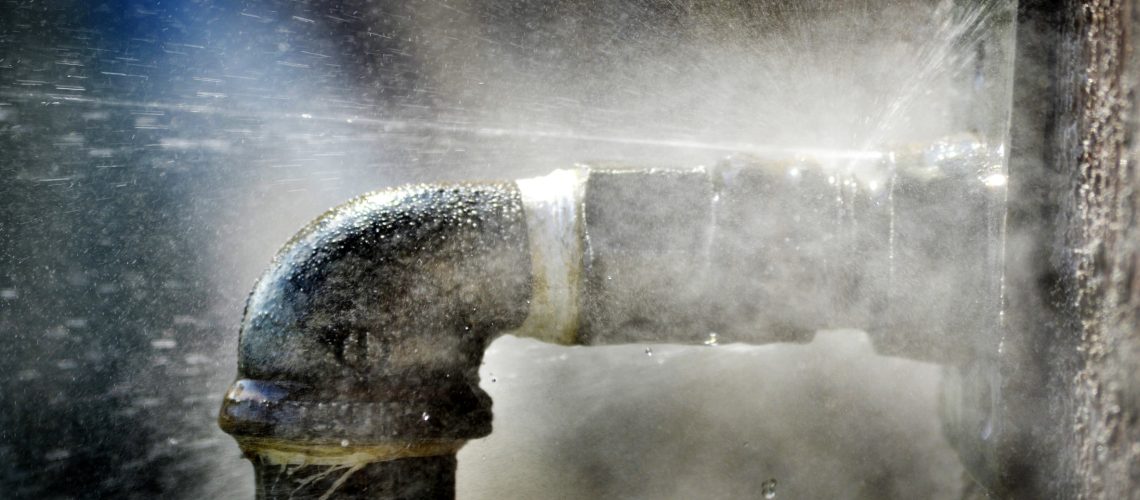 Old rusty pipe with leak and water spraying out into the air as a major plumbing problem