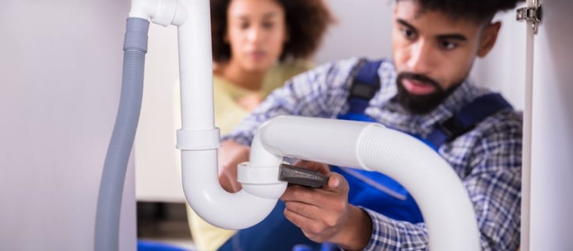 Plumber in blue repairing a white sink pipe
