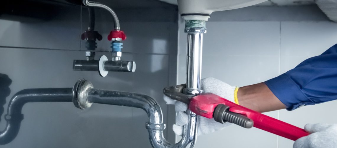 Plumber hands holding wrench doing repairing work at the sink and clogged pipe in bathroom carefully